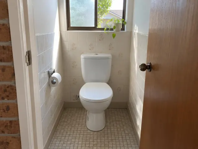 Clean white toilet in a small tiled bathroom with a window and timber door in Bangor