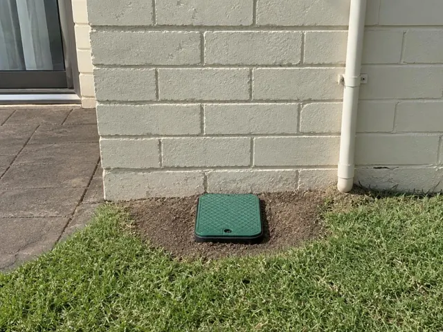 Green capped sewer access opening beside a house wall and lawn in Bangor